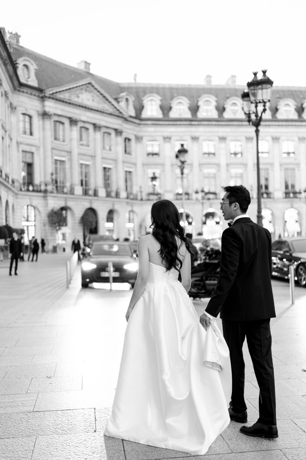 Black and white photo of a bride and groom holding hands in front of an elegant Parisian building.