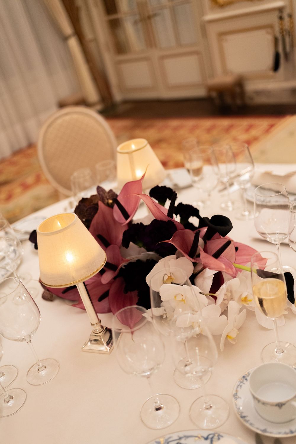 Elegant wedding reception table with pink and black floral centerpiece, candles, and crystal wine glasses on white linen.