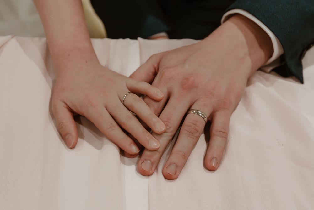 Newlywed couple holding hands showing wedding rings on white dress background.