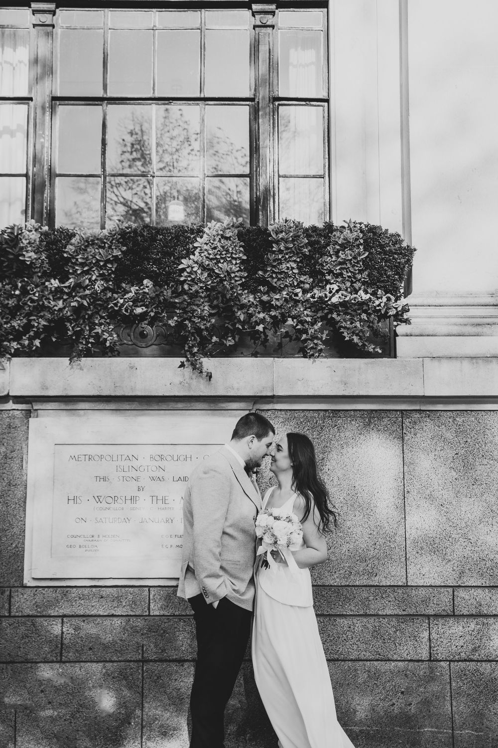 Black and white photo of a bride and groom sharing a romantic moment outside an elegant stone building.