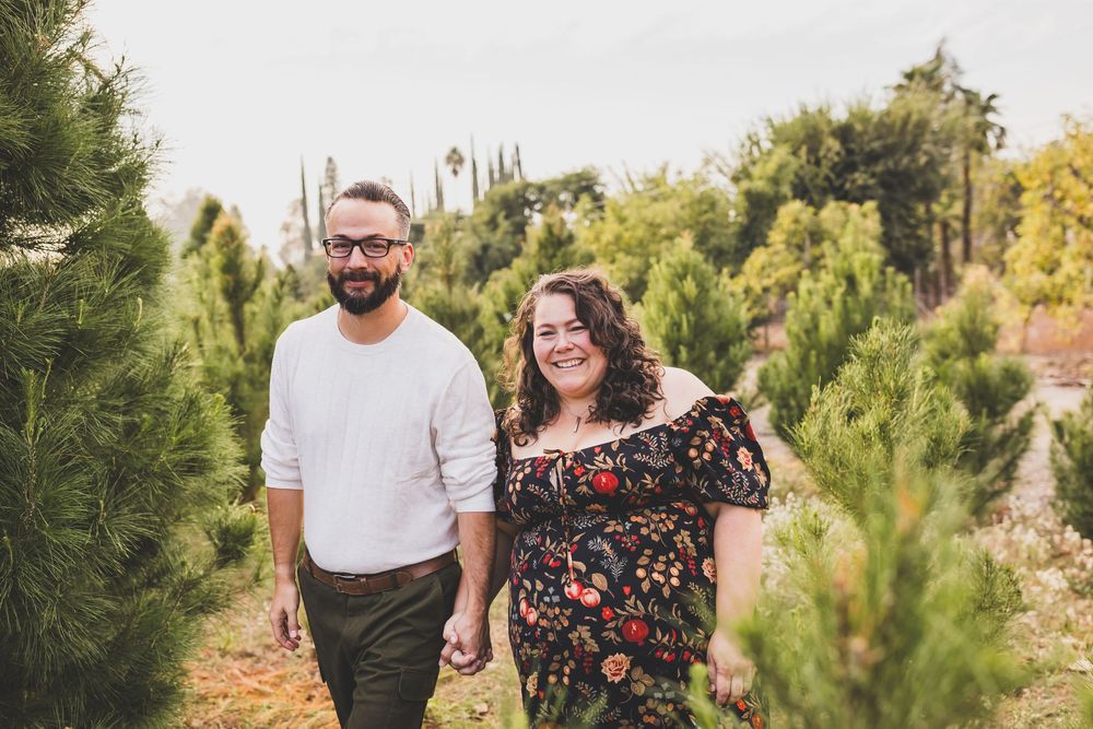 Couple holding hands and smiling while walking through a lush Christmas tree farm outdoors during a mini session near yucaipa ca