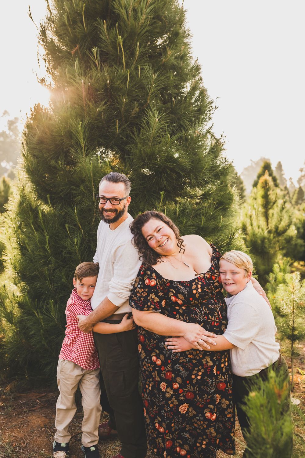 Family of four smiling together at a Christmas tree farm during golden hour sunset.