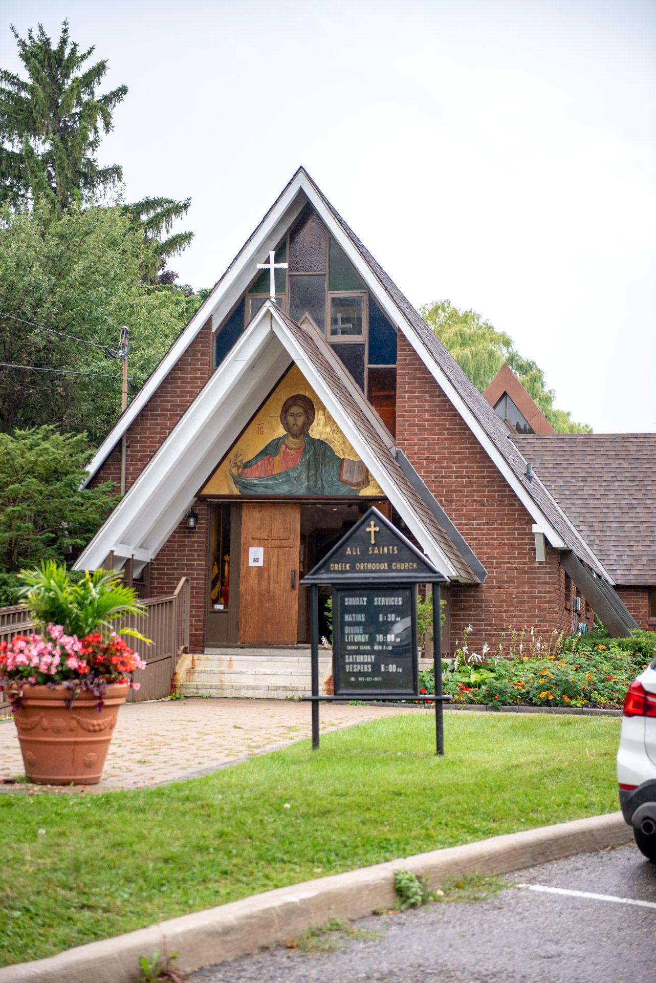 Greek Orthodox church exterior with A-frame roof, religious mosaic above entrance, and brick facade.