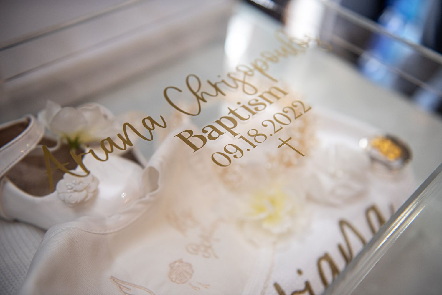 Gold engraved baptism keepsake box for Ariana Christopoulos dated 09.18.2022 with white baby shoes.