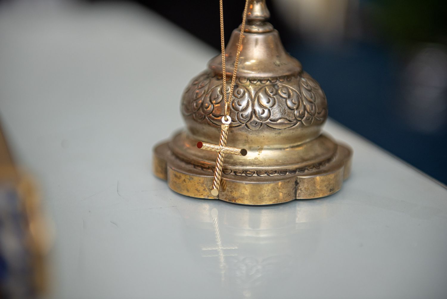 Ornate antique brass baptism censer with a delicate gold cross necklace on a white surface.