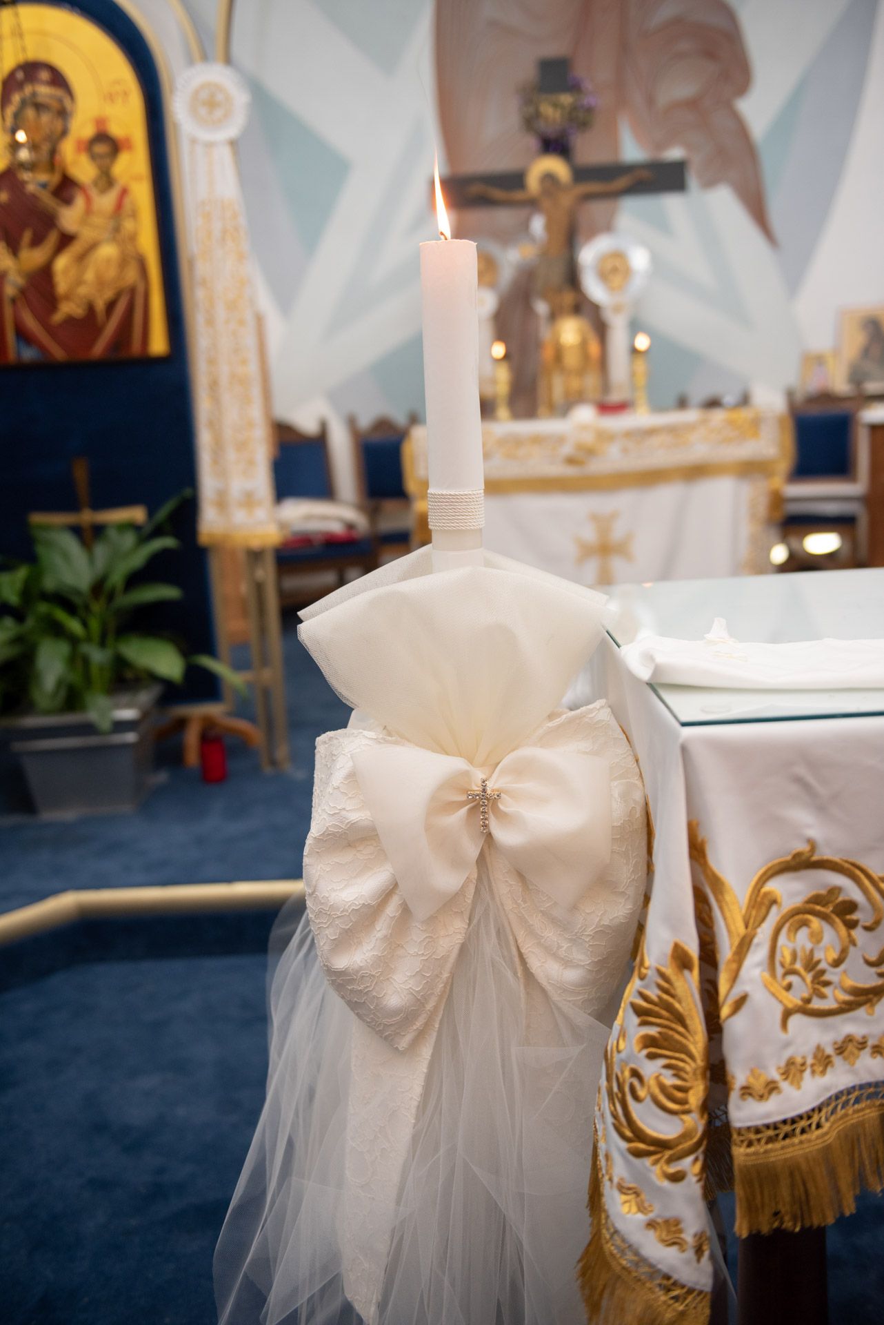 White baptism candle with ivory bow and tulle decoration on altar in Orthodox church.