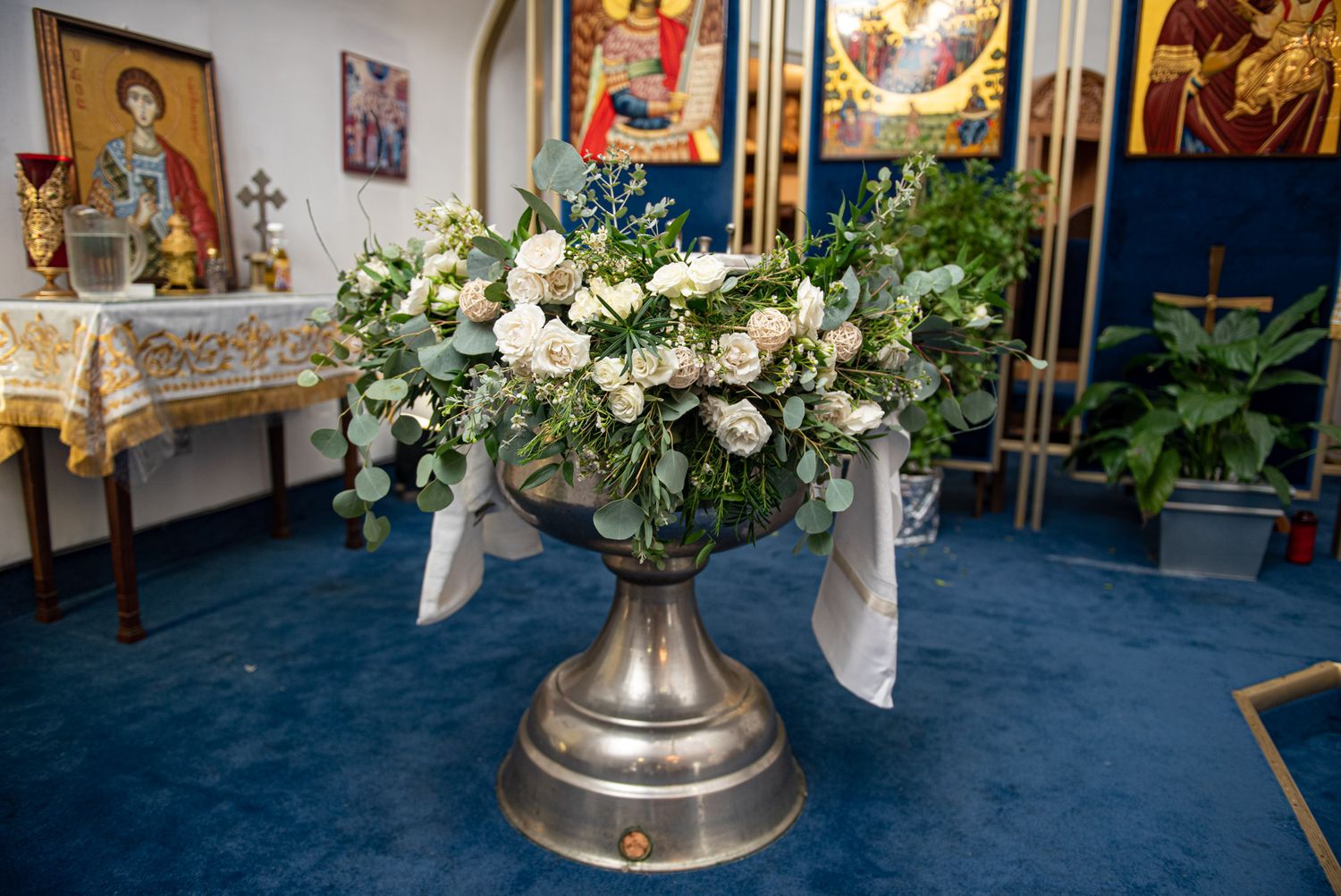 Elegant silver baptismal font decorated with white roses and greenery floral arrangement in church.