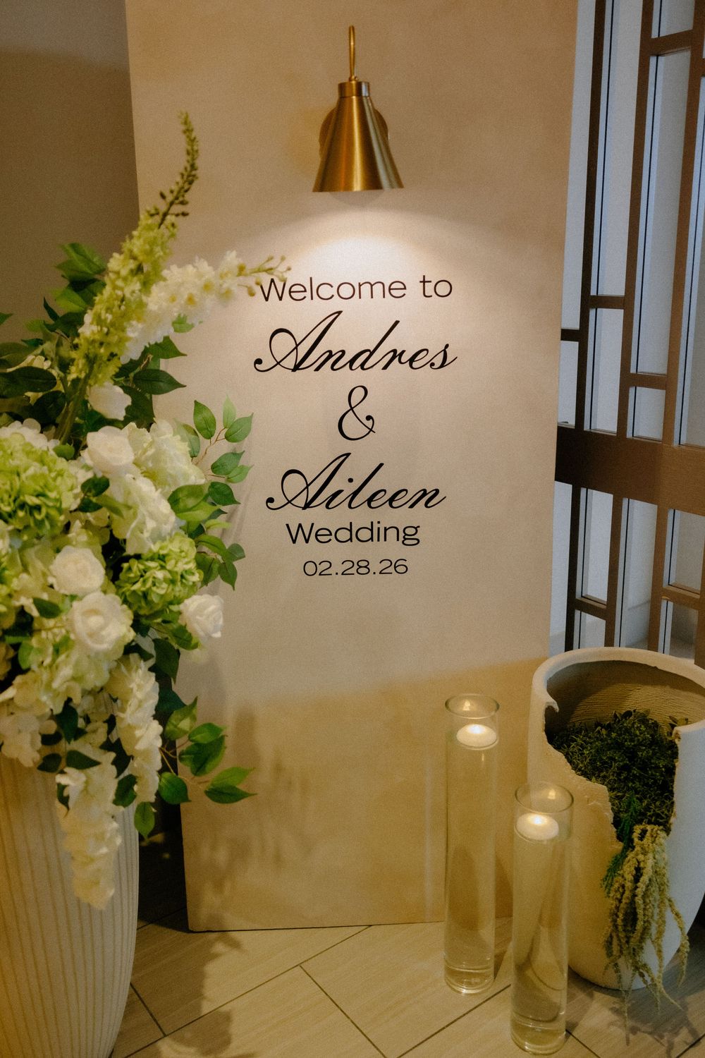 Elegant wedding welcome sign for Andres and Aileen on 02.28.26, adorned with white floral arrangements and candlelight.
