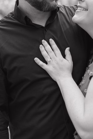 Black and white photo of a couple embracing, showcasing a diamond engagement ring on the woman's hand.