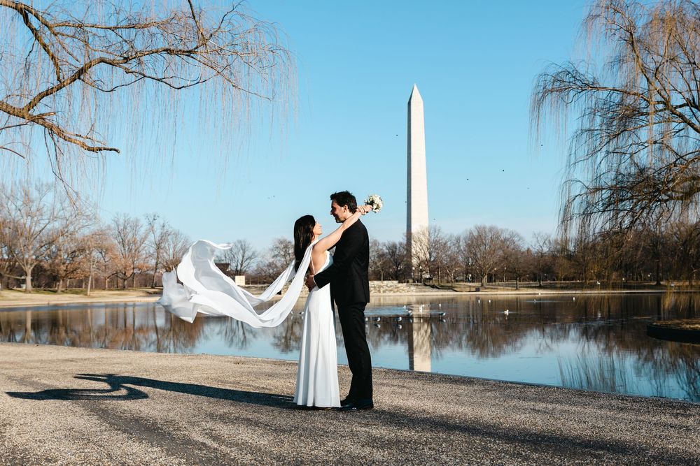 Bride and groom kissing near the Washington Monument reflecting pool on a clear sunny day.