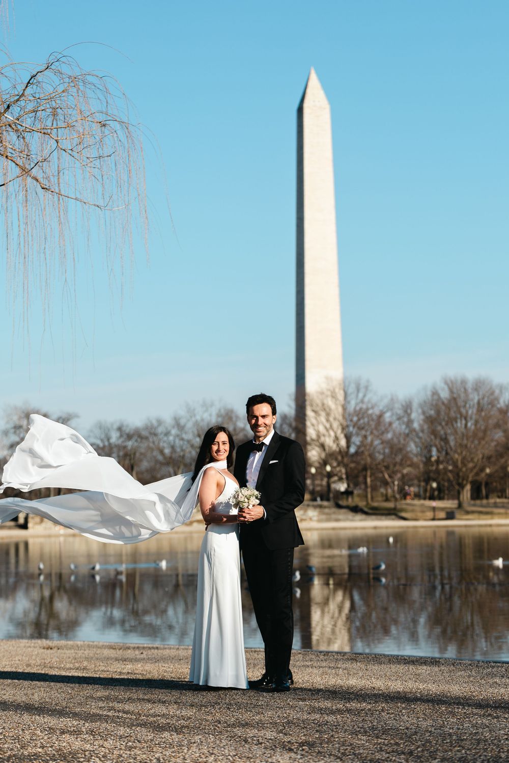 Bride and groom pose by the Reflecting Pool with the Washington Monument in Washington DC on their wedding day.