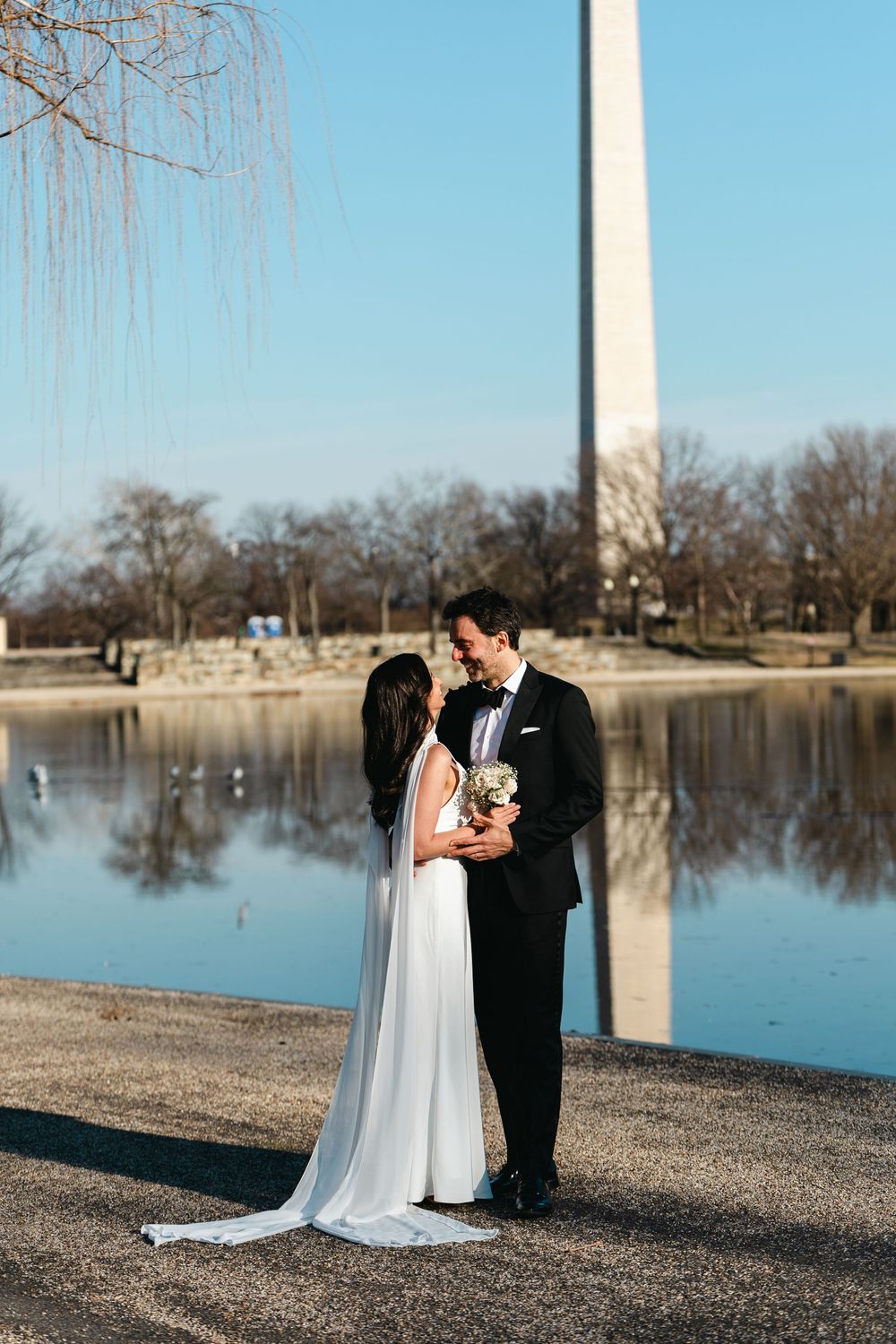 Bride and groom share a romantic moment by the Tidal Basin with the Washington Monument reflected in the water.