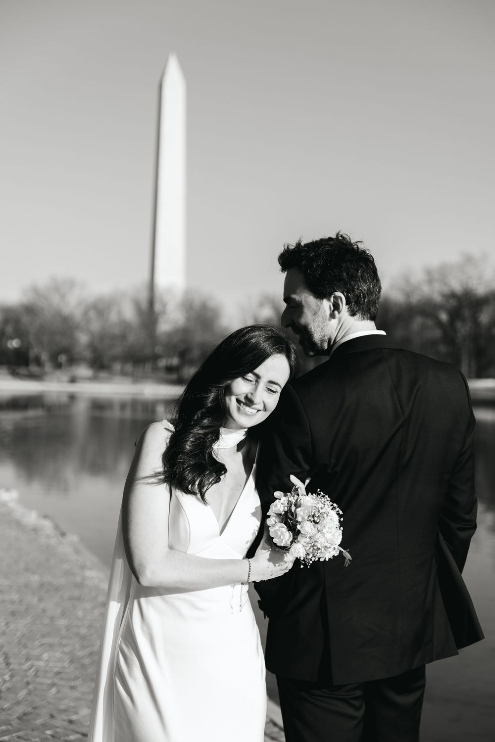 Black and white photo of bride and groom embracing near the Washington Monument reflecting pool.