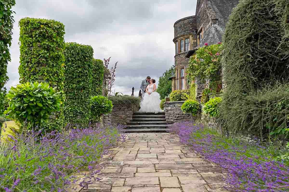 Bride and groom kissing on stone steps surrounded by lavender and lush gardens at a historic castle wedding venue.