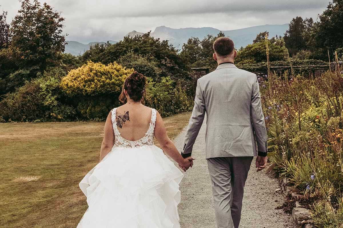 bride and groom walk hand in hand with the Lake District in the distance