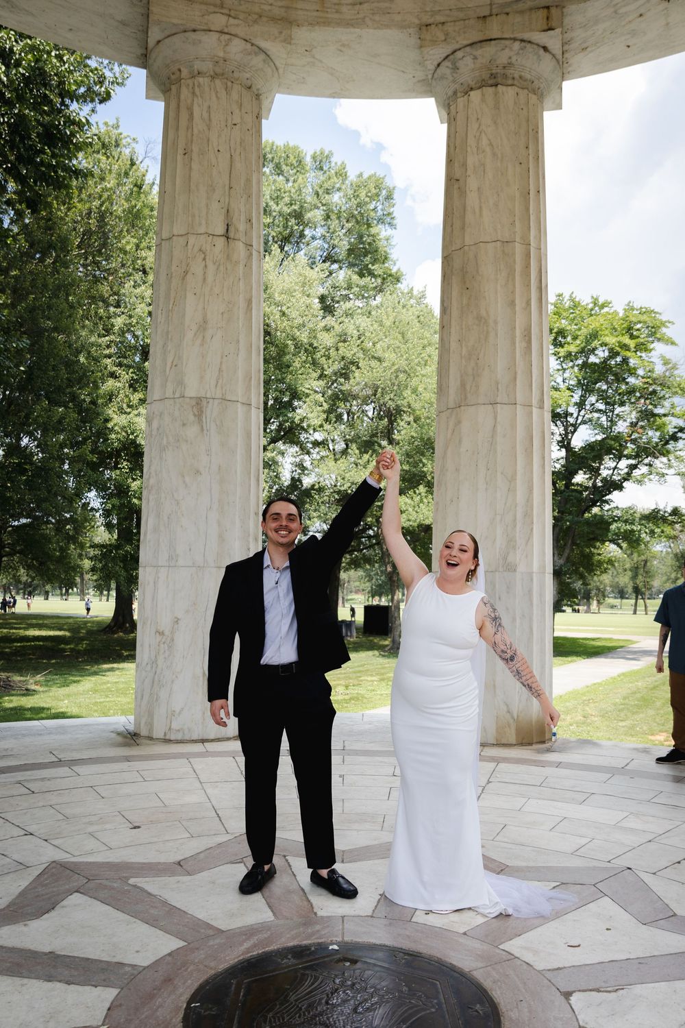 Joyful newlyweds celebrate raising hands after wedding ceremony at DC memorial with marble columns.