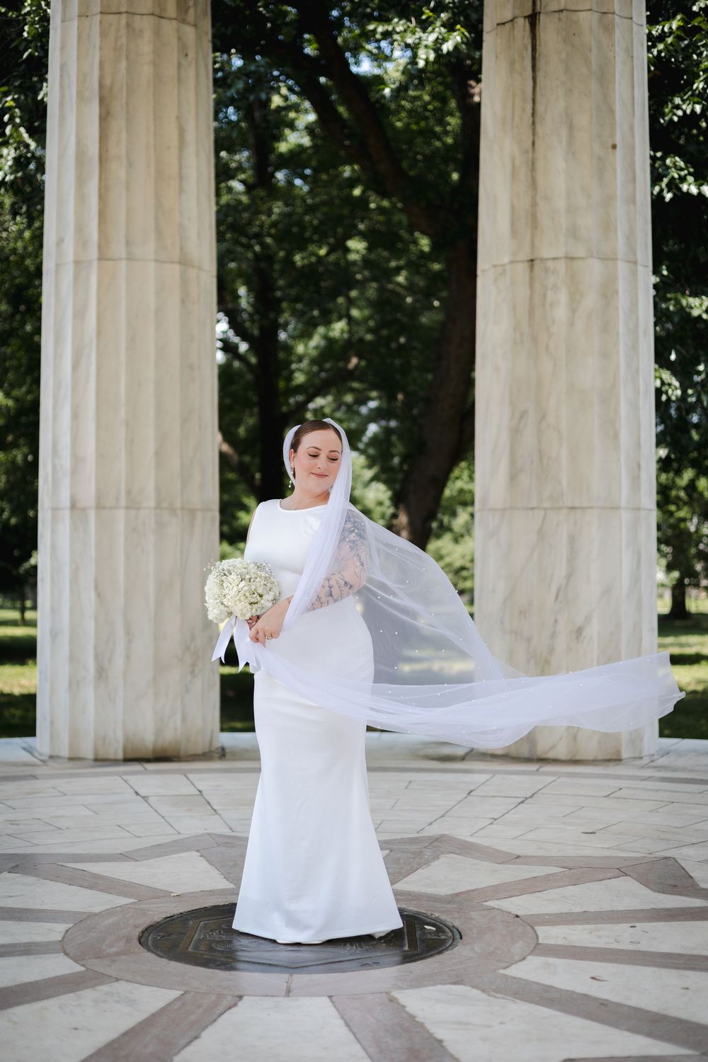 Bride in white gown with flowing veil poses at DC memorial columns.