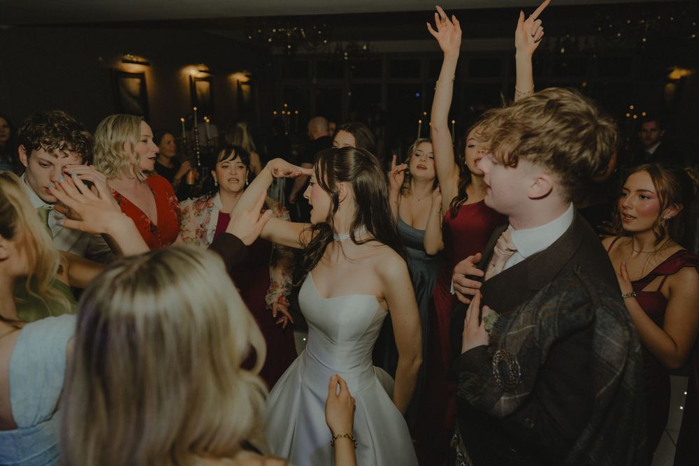 Bride and groom dancing joyfully with guests at a lively wedding reception party.