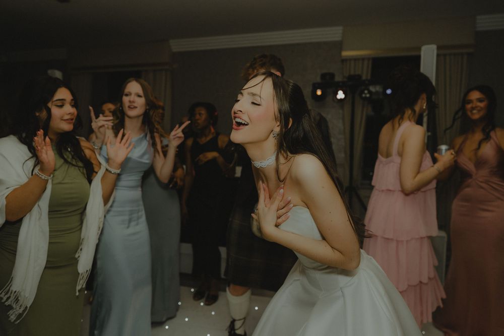 Bride laughing and dancing joyfully with bridesmaids in colorful gowns at a lively wedding reception.