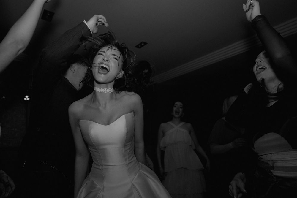 Black and white photo of a bride dancing ecstatically with guests at her wedding reception.