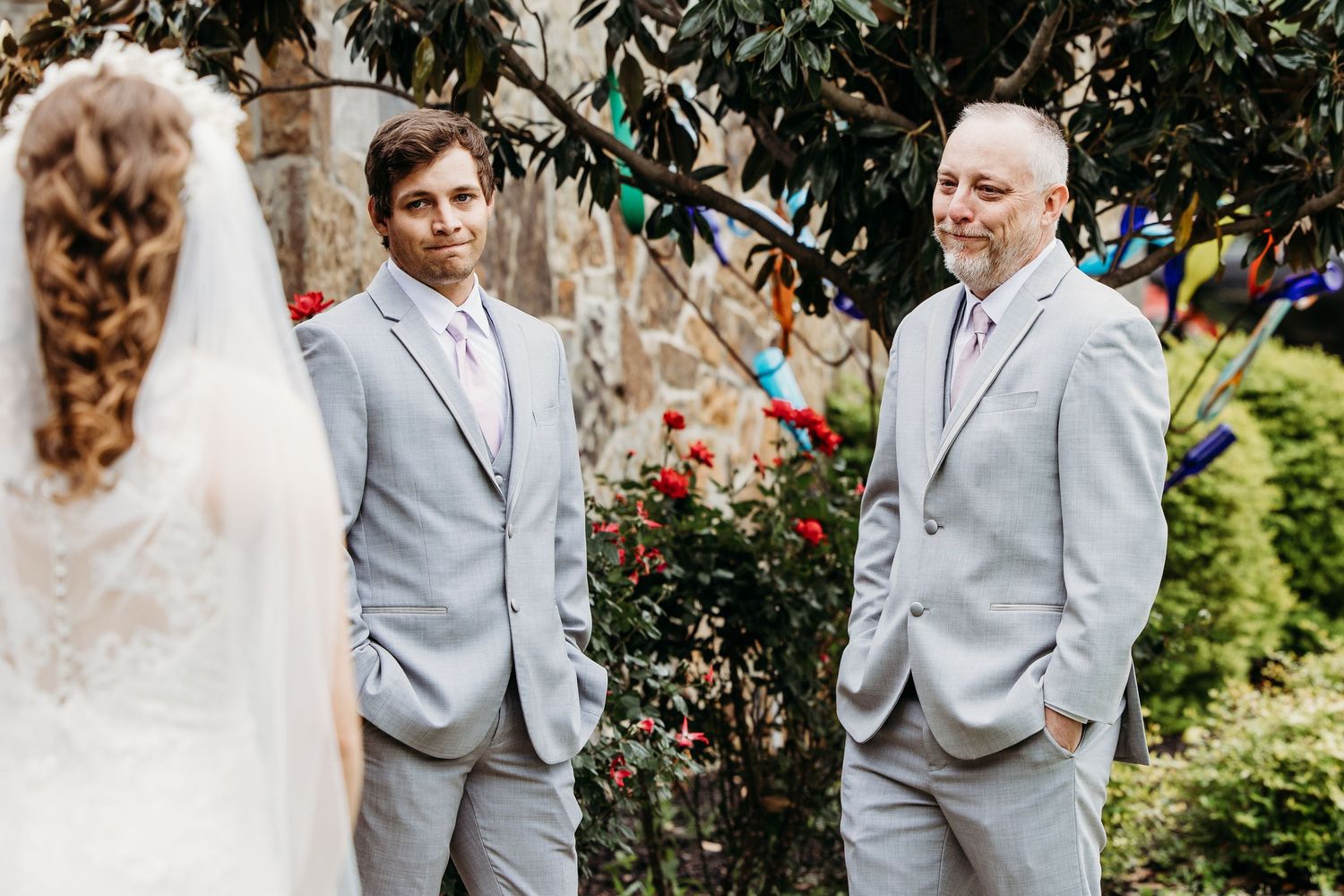 Two groomsmen in light gray suits stand outdoors during a wedding ceremony with colorful bunting decorations in DFW.