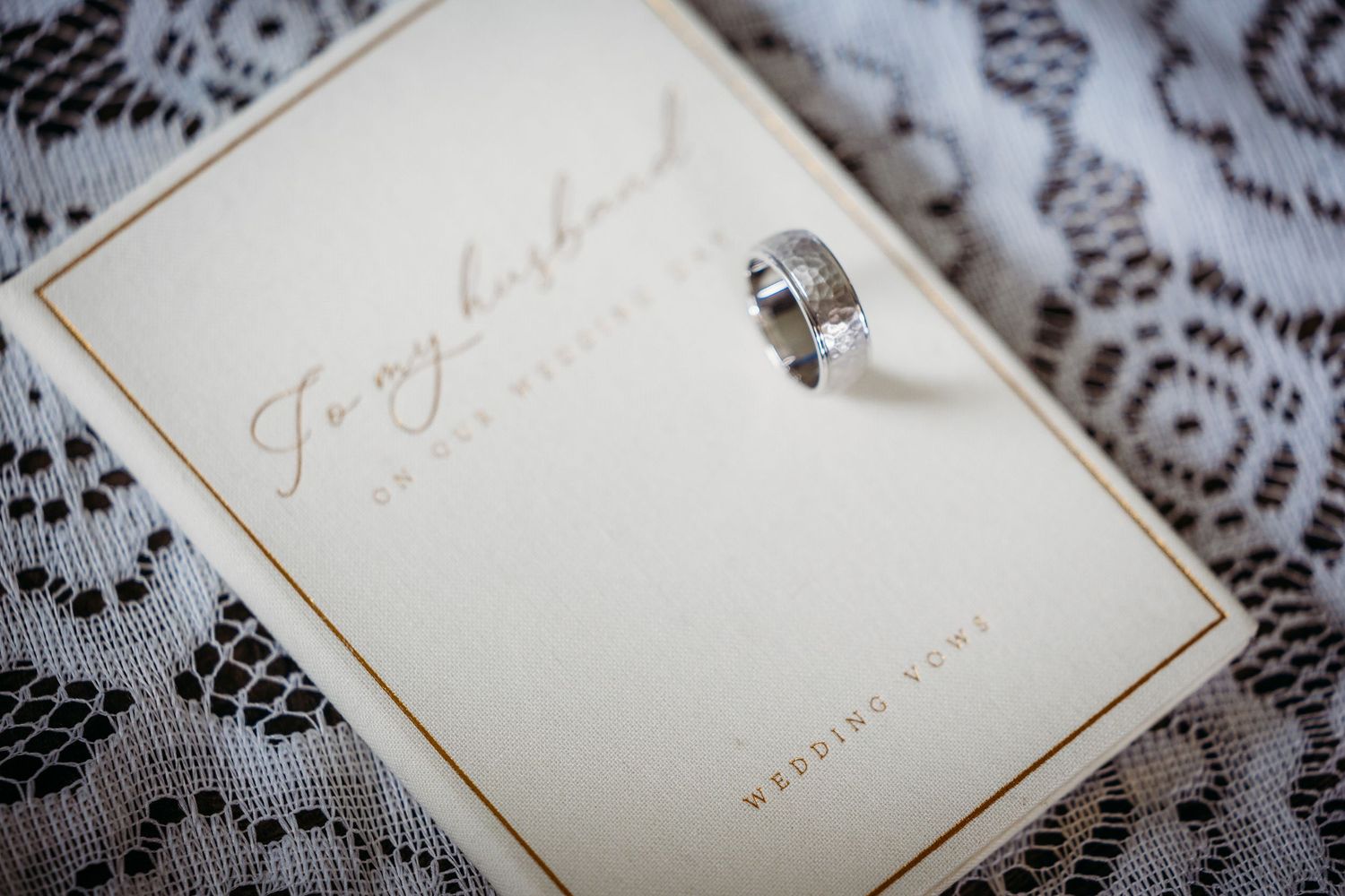 Silver wedding band resting on a wedding vows card addressed to husband, placed on delicate white lace fabric in Fort Worth.