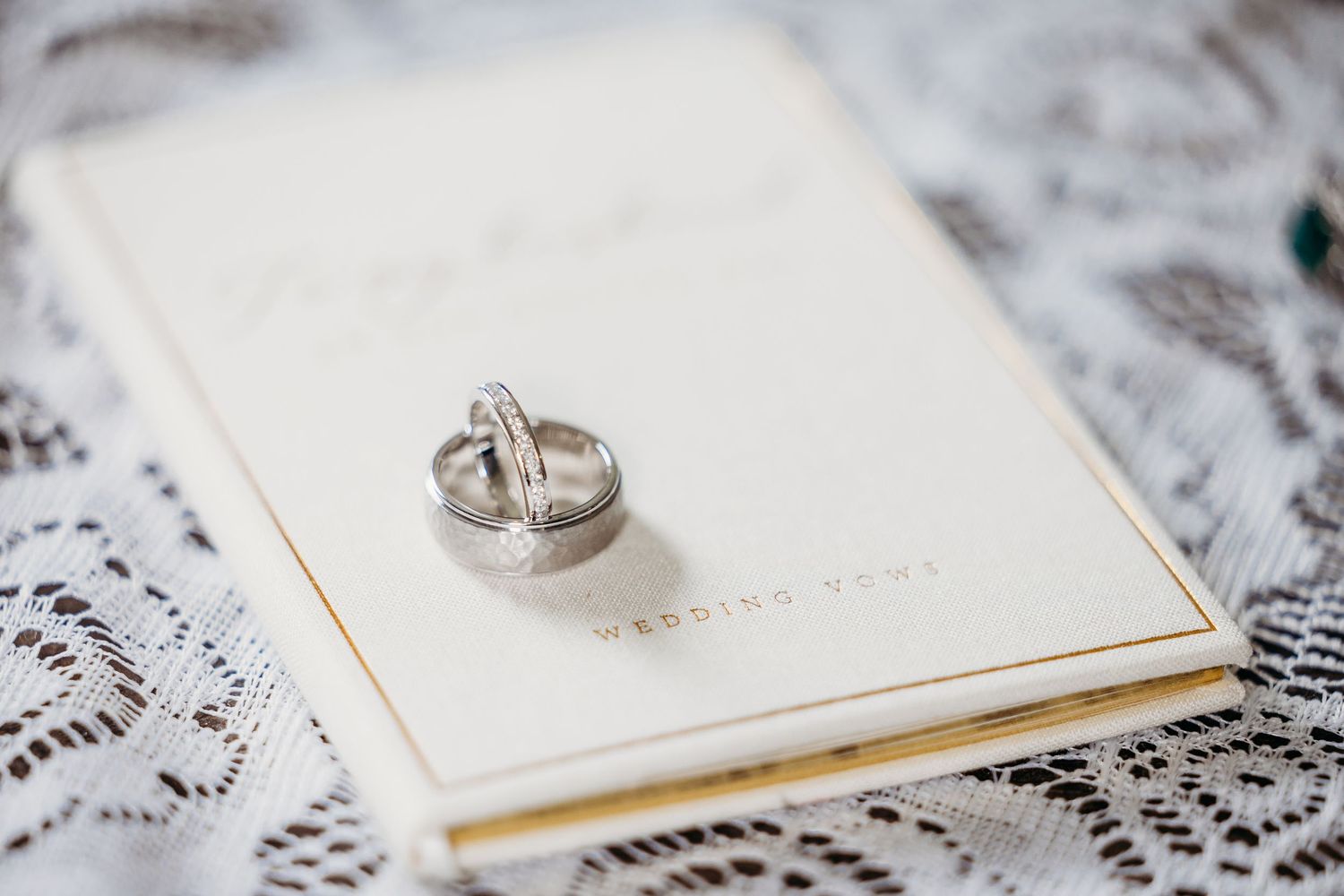 Two silver wedding rings resting on a gold-trimmed wedding vows booklet atop delicate white lace fabric in Fort Worth.