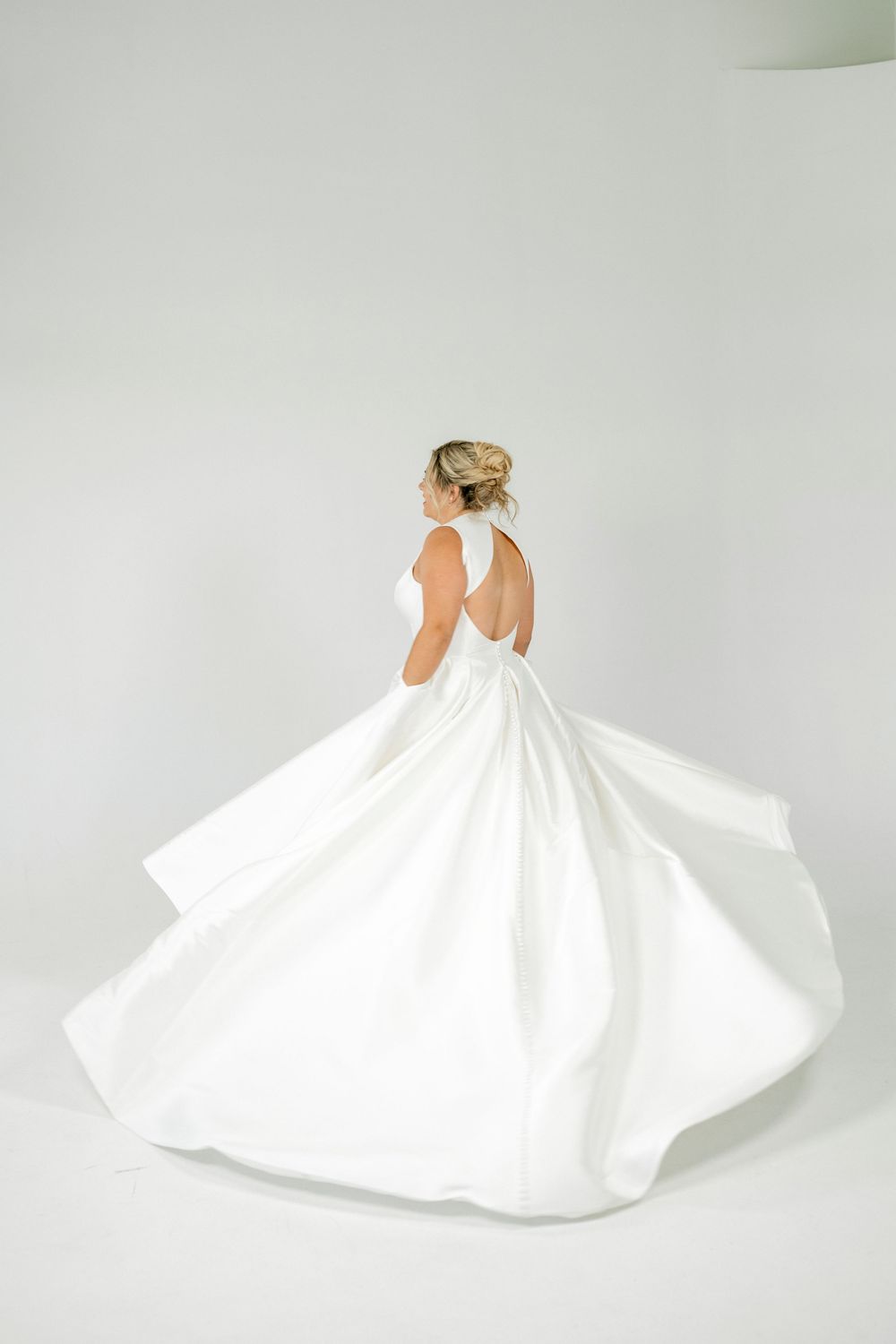Bride in elegant white ball gown with open back, twirling in studio.