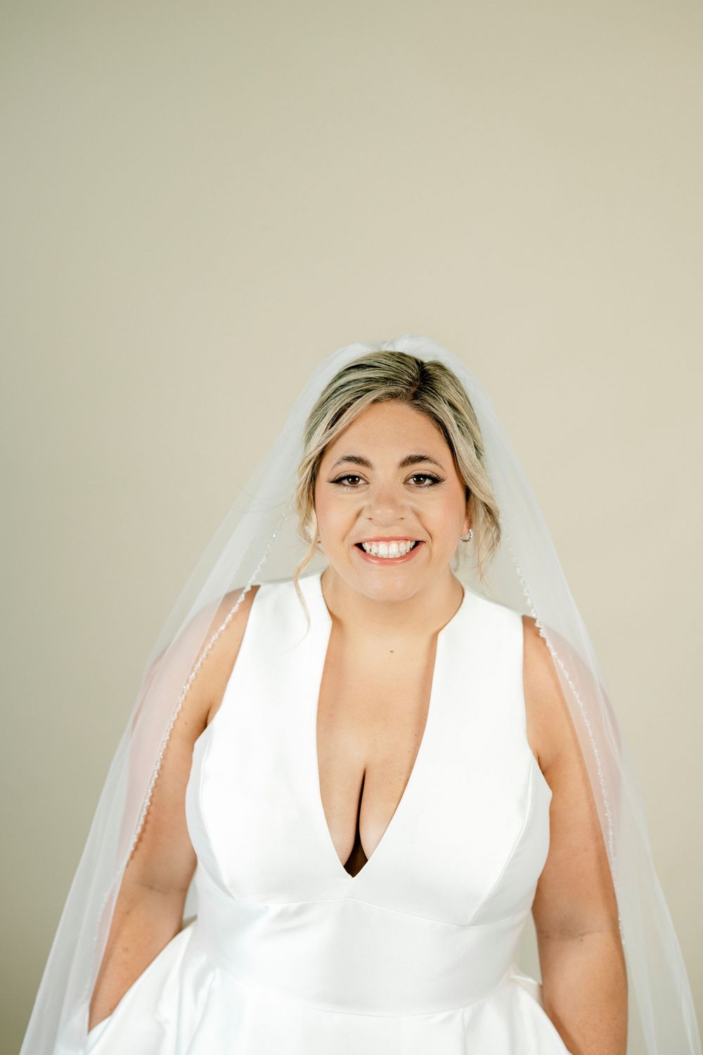 Happy bride in deep V-neck white wedding dress wearing long cathedral veil, smiling.