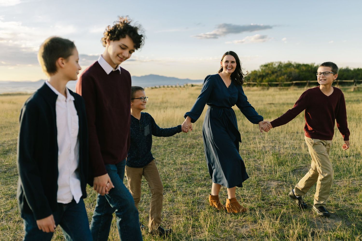 Happy family of five holding hands and walking together through a scenic open field at sunset. Tunnel Springs, Utah family photos