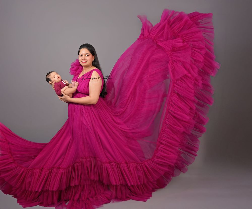 Woman in flowing magenta ruffle gown holding newborn baby in matching outfit during professional studio photoshoot.