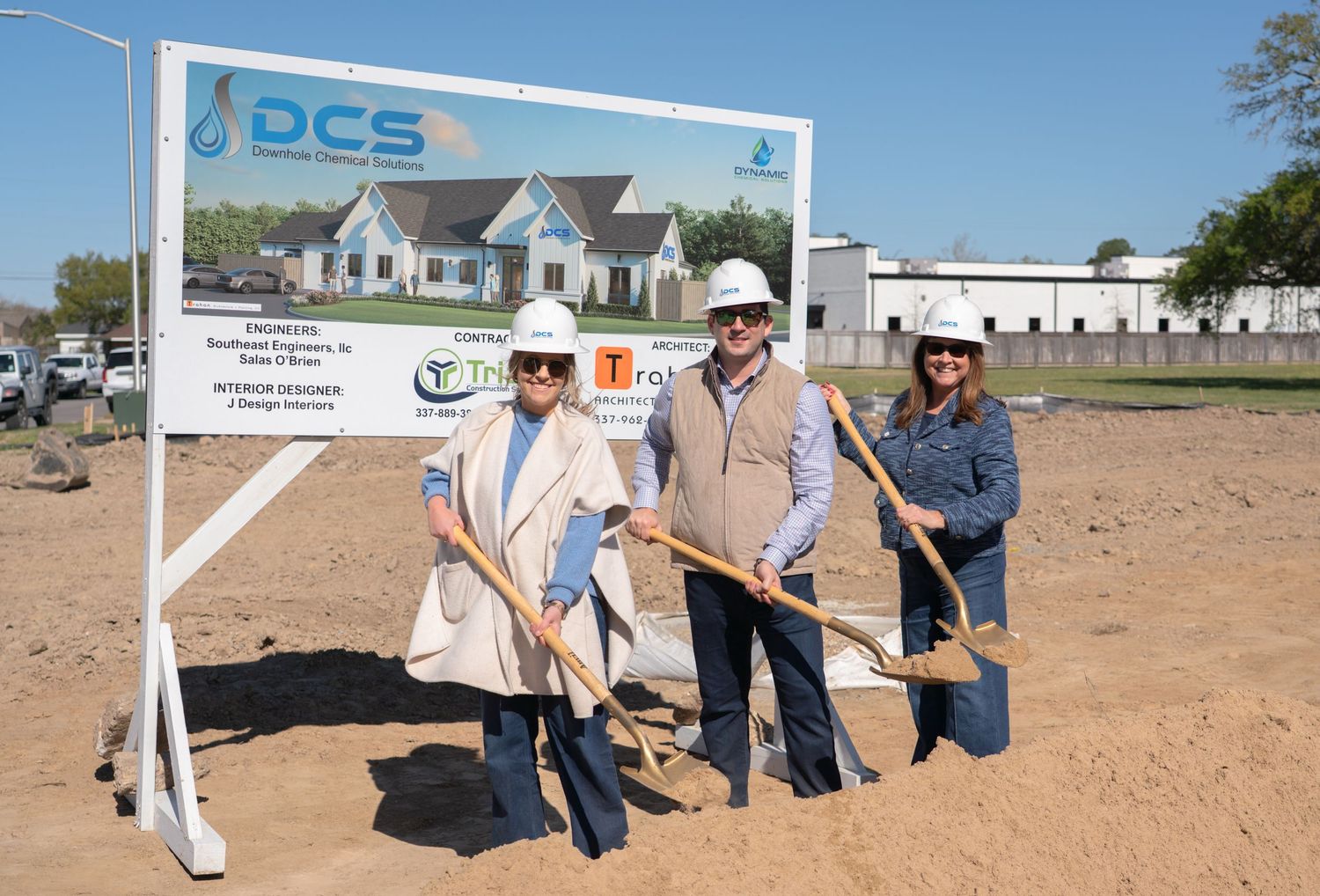Three people pose with golden shovels at a DCS groundbreaking ceremony on a sunny day.