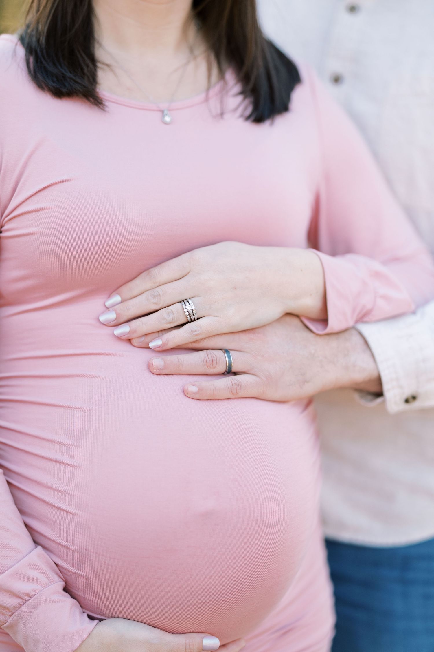Close-up of pregnant woman in pink dress with partner's hand on her baby bump.