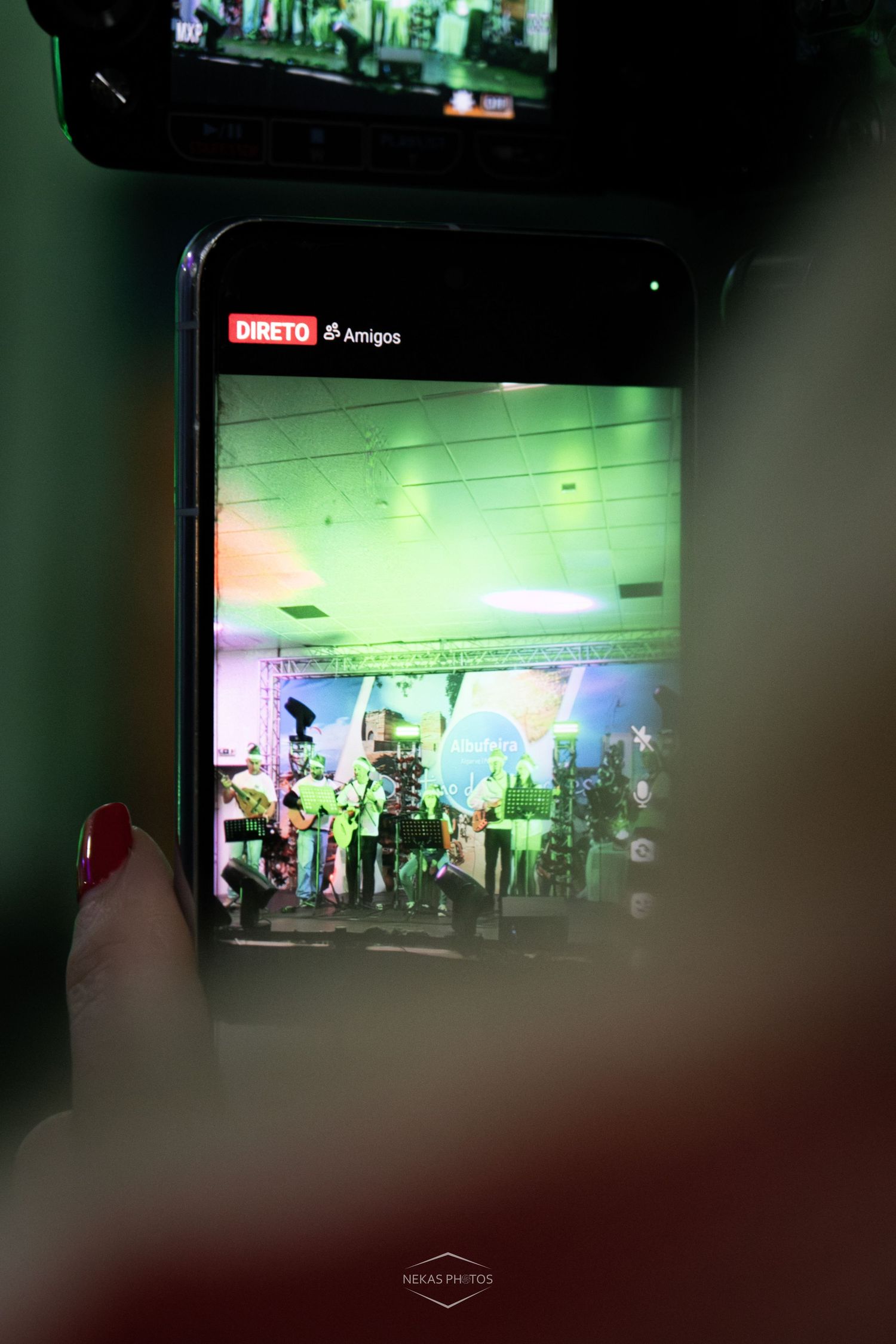 Person holding smartphone filming a live concert stage with green lighting, displaying a live stream labeled DIRETO.