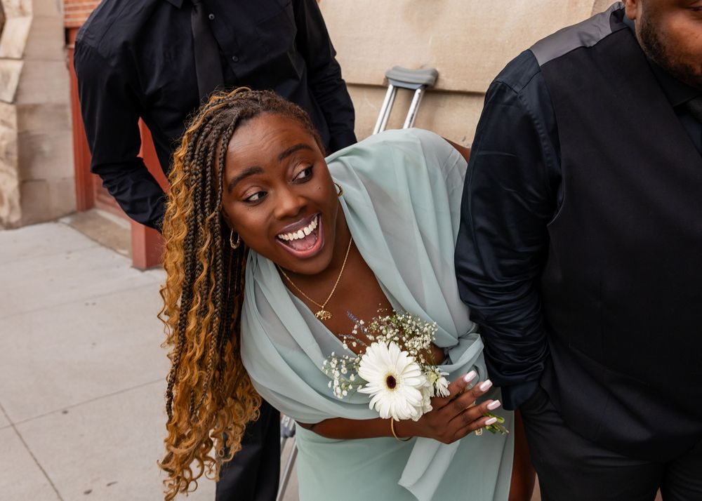 Smiling young woman in mint green dress holding white flower corsage at a formal event outdoors.