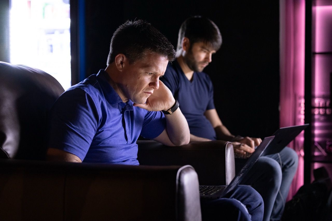 Russell Brunson& Todd Dickerson working on their laptops backstage with pink background light at FHL in Nashville.