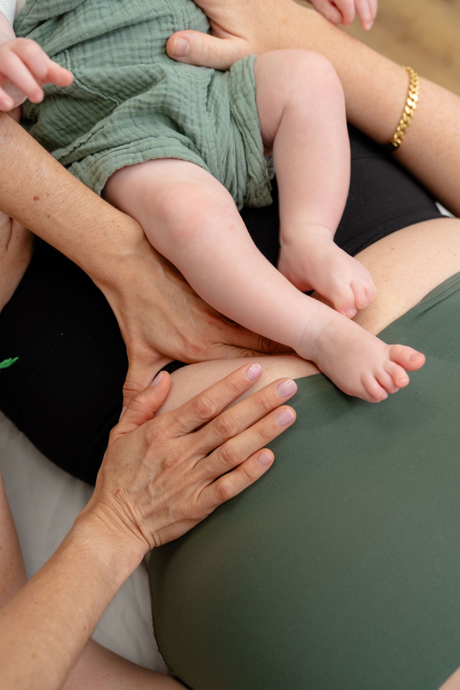 Adult hands gently massaging a newborn baby's legs during an infant massage therapy session.