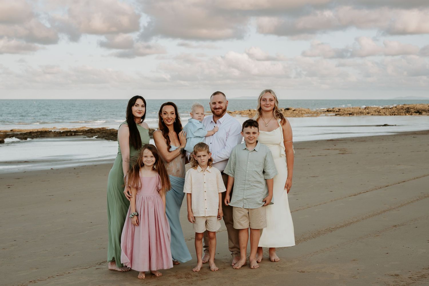A family group stands together on a cloudy beach with waves and rocks in the background.