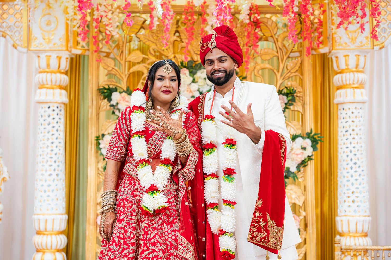 A traditional Indian wedding ceremony with the couple in red and white attire surrounded by ornate golden decor.
