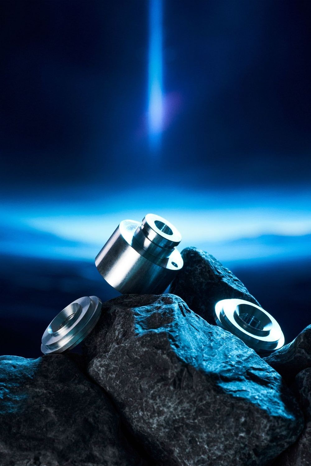 Metal vaping atomizers displayed on dark rocks against a dramatic blue backlit background.