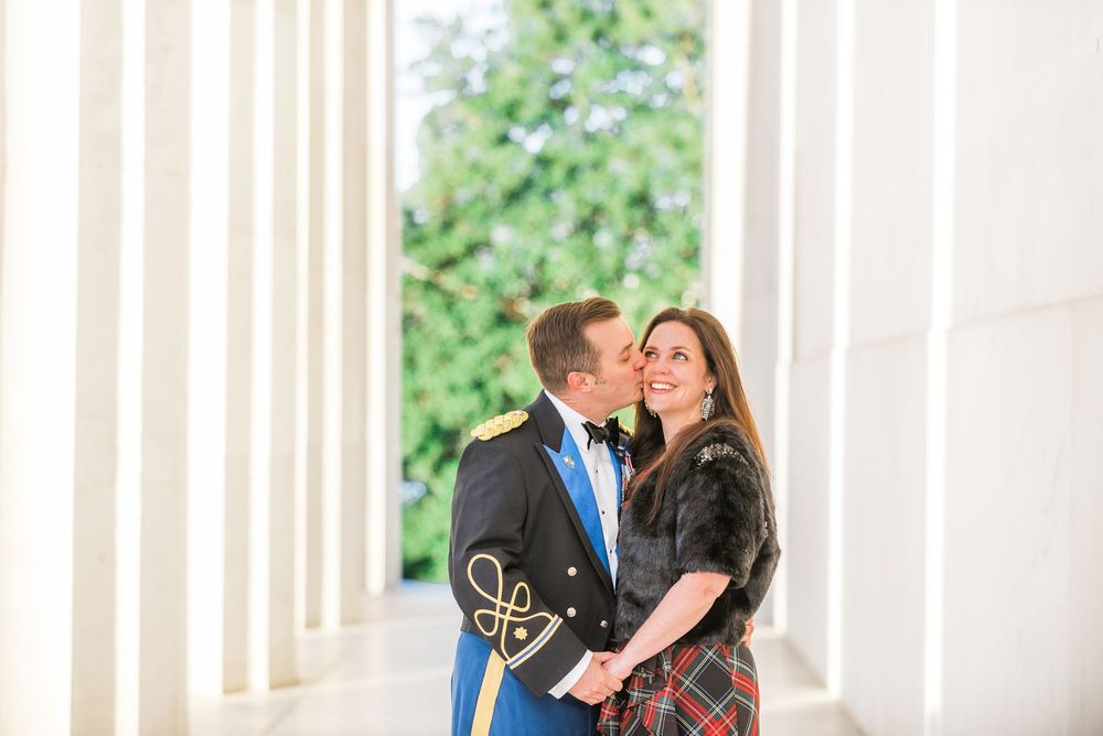 A couple shares an intimate moment between classical white columns.