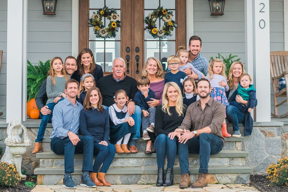 Extended family gathering on front porch steps of a blue house decorated for the holidays.
