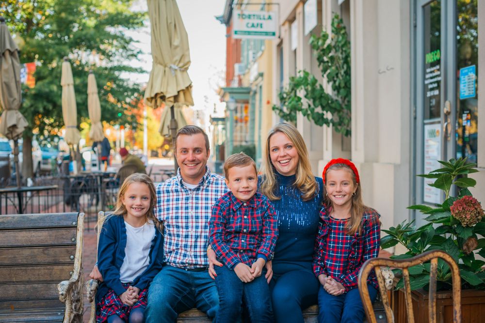 Happy family of five smiling together on a outdoor bench in a charming downtown shopping district.