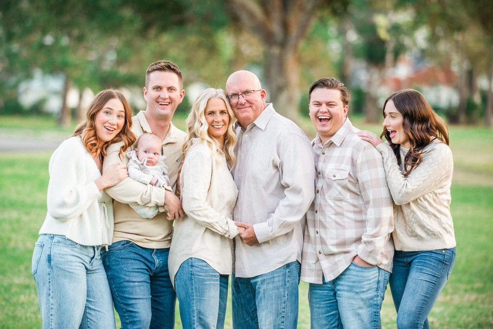 A group wearing coordinated cream sweaters embraces while laughing together outdoors.