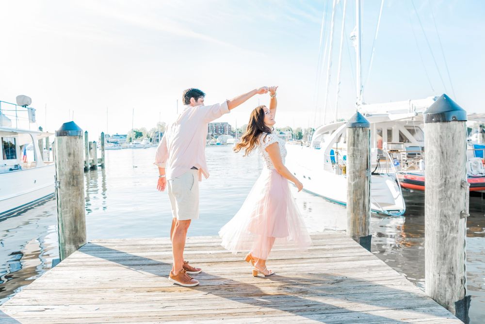 A couple dances together on a wooden dock surrounded by boats and marina posts.