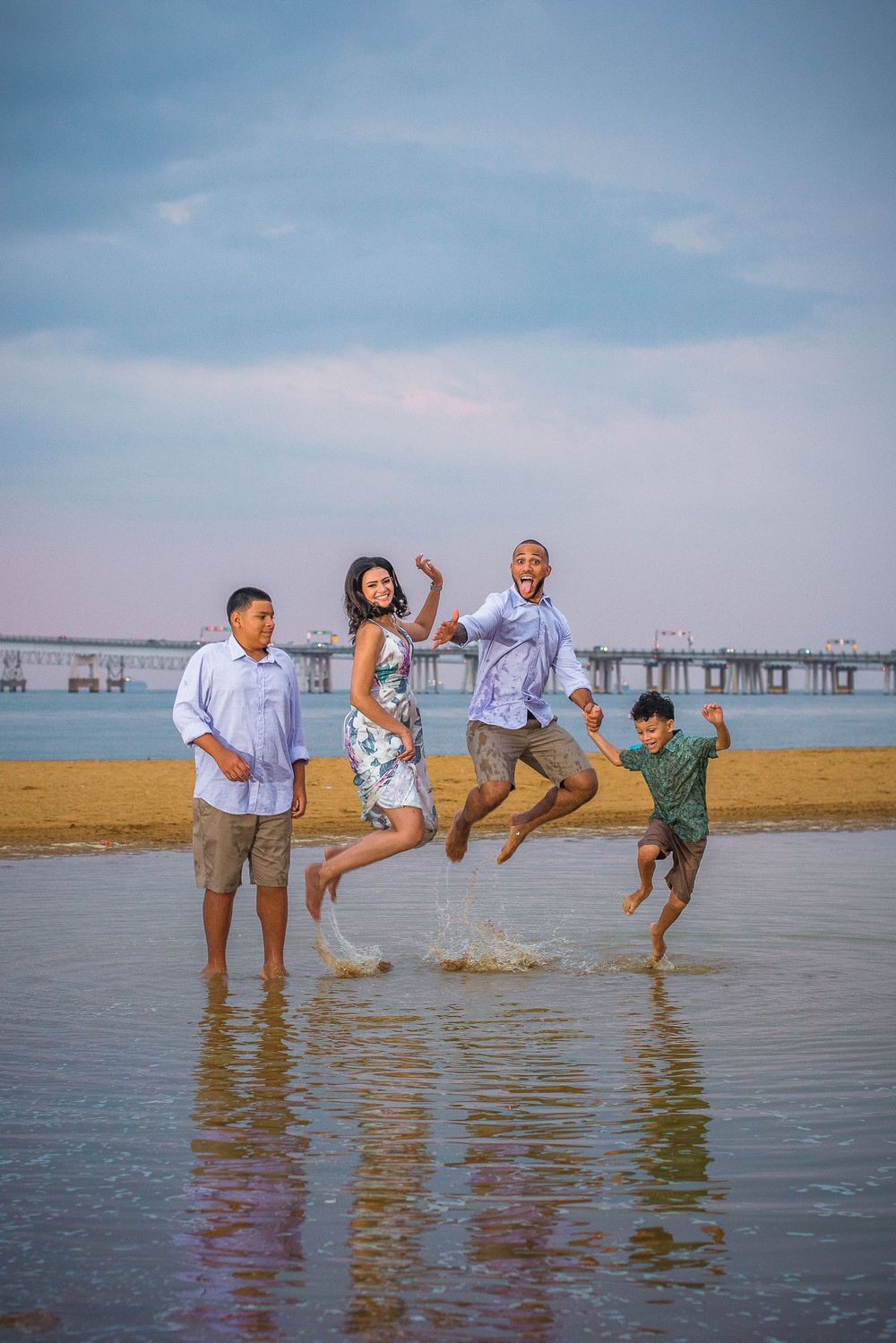 A joyful group jumps together at the beach during sunset with a pier in the background.