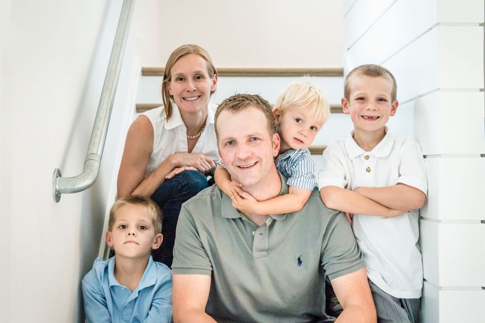 A family poses together on white stairs inside their home.