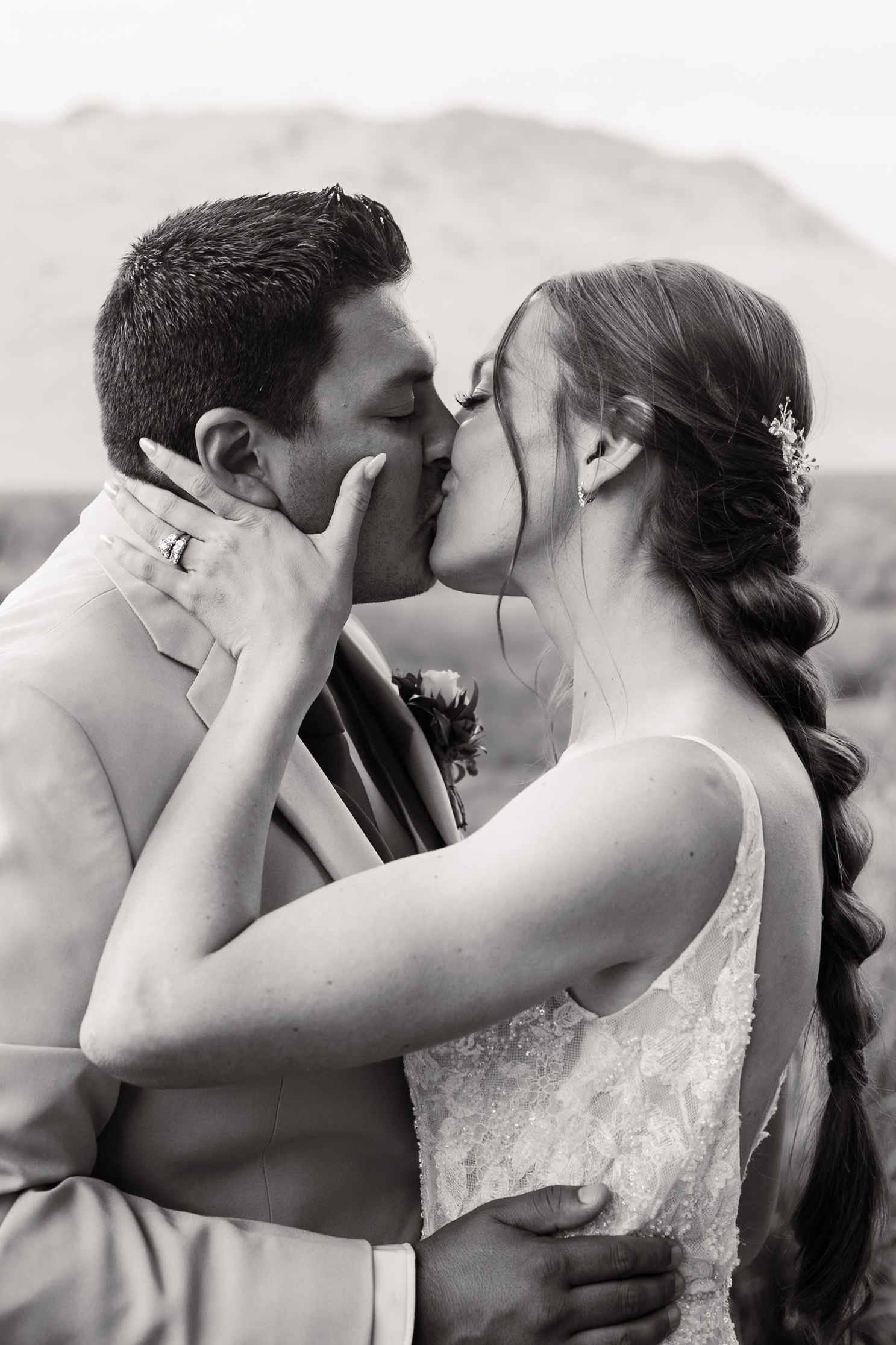 A romantic black and white wedding photo shows a couple sharing a tender kiss against a mountain backdrop.