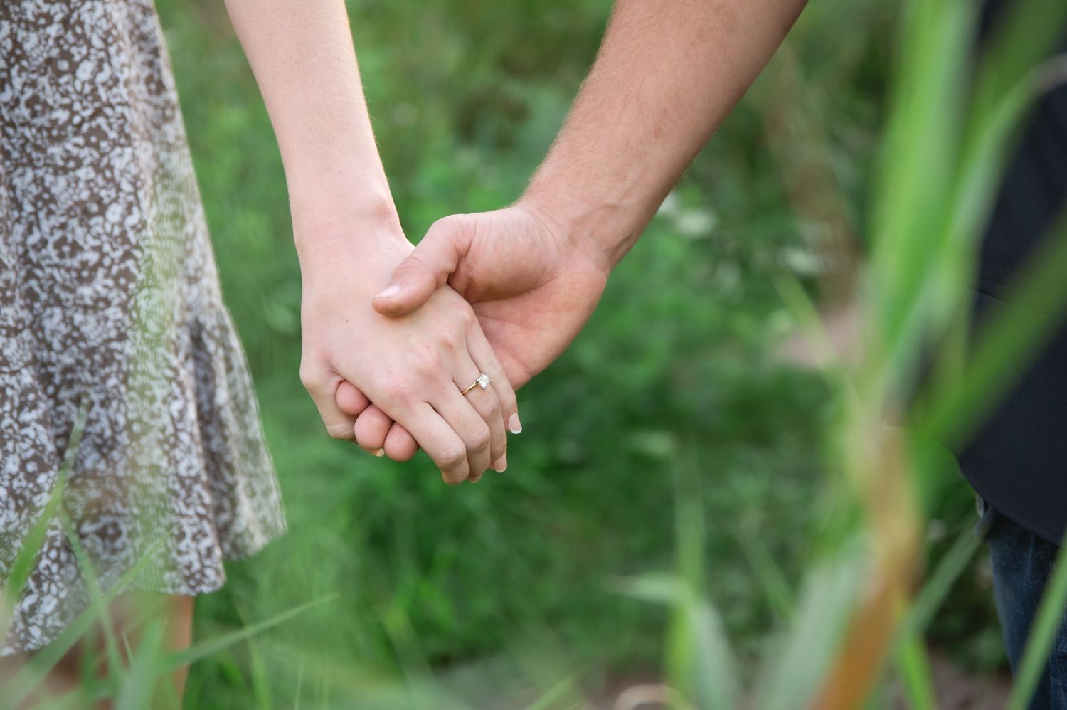 Two people hold hands while standing in a garden with green foliage in the background.