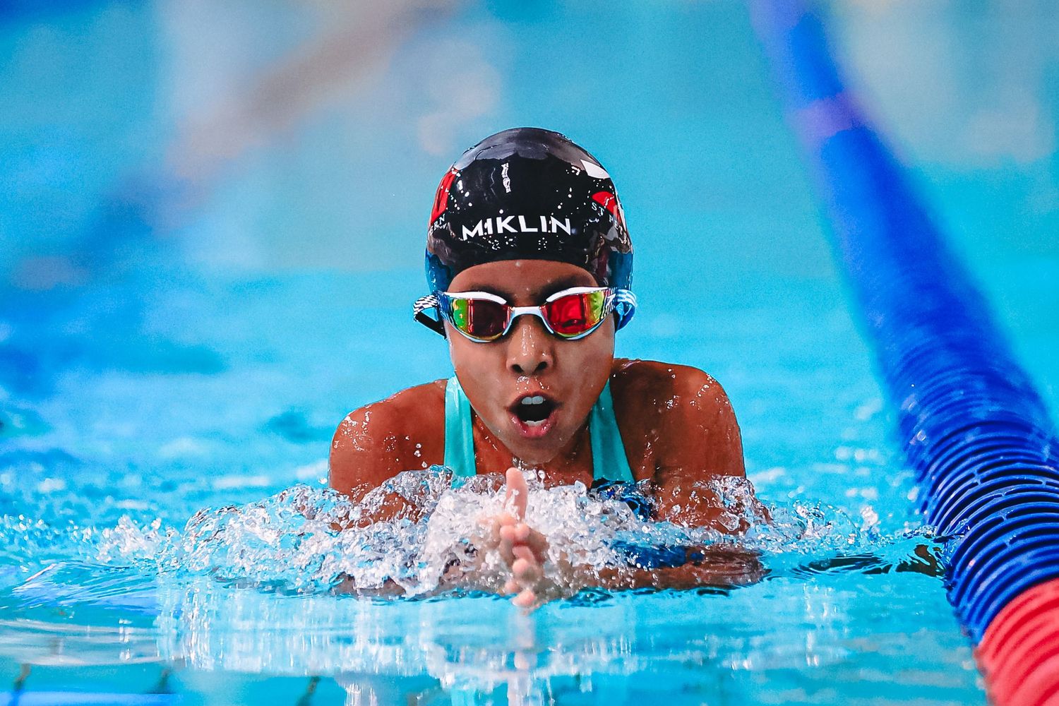 A competitive swimmer glides through the pool during a race with water splashing around them.